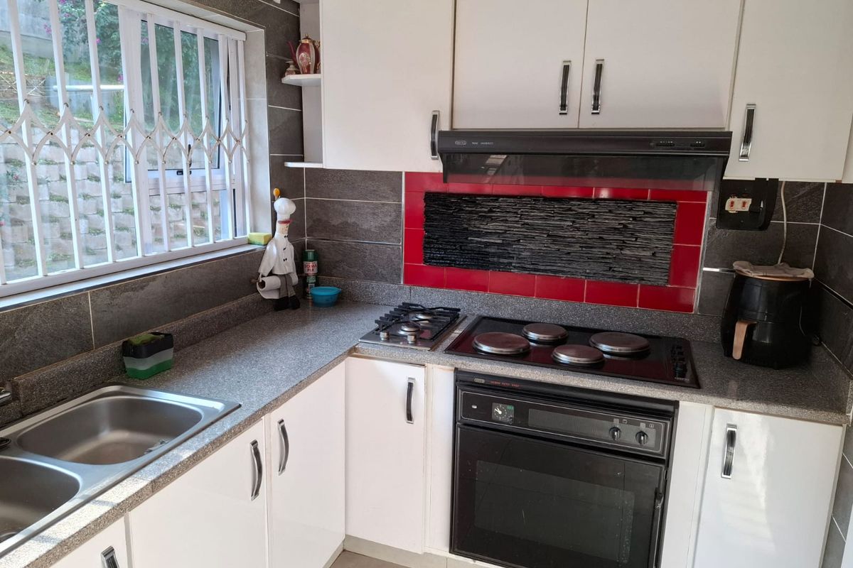 A functional kitchen featuring white cabinetry, a combination gas and electric hob, built-in oven, extractor fan, and a stainless steel double sink.
