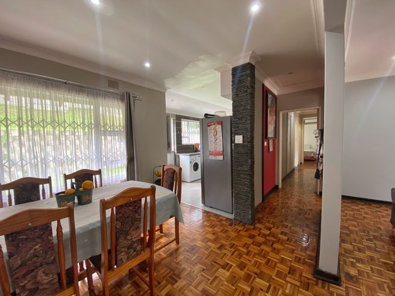 Open-plan living and dining area featuring classic parquet flooring, a stone-clad feature pillar, and recessed downlighting, leading towards a functional kitchen space.