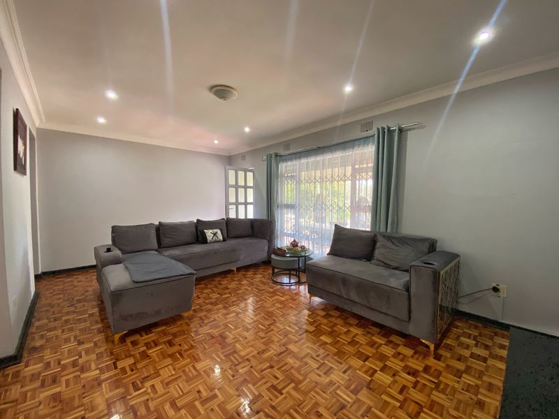 A well-maintained living room featuring classic parquet flooring, recessed downlighting, and decorative cornicing, providing a warm and inviting atmosphere.