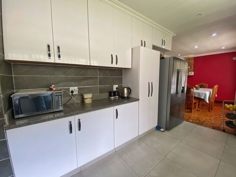 Modern kitchen featuring white cabinetry, stone countertops, and a tiled backsplash, seamlessly flowing into the adjacent dining area.