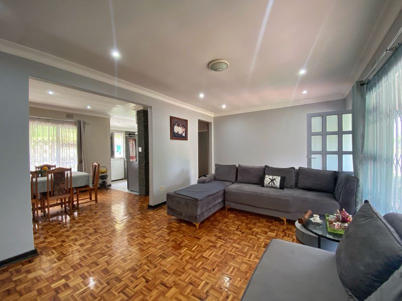Spacious open-plan living and dining area featuring polished parquet flooring, modern recessed lighting, and a decorative stone-clad pillar.
