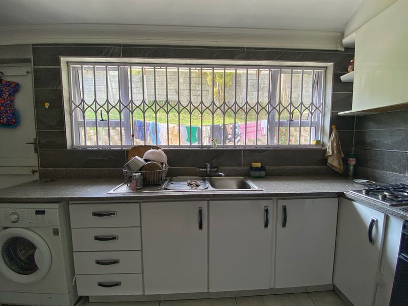 A functional kitchen featuring white cabinetry, laminate countertops, a stainless steel sink, and a built-in hob with a window security gate.