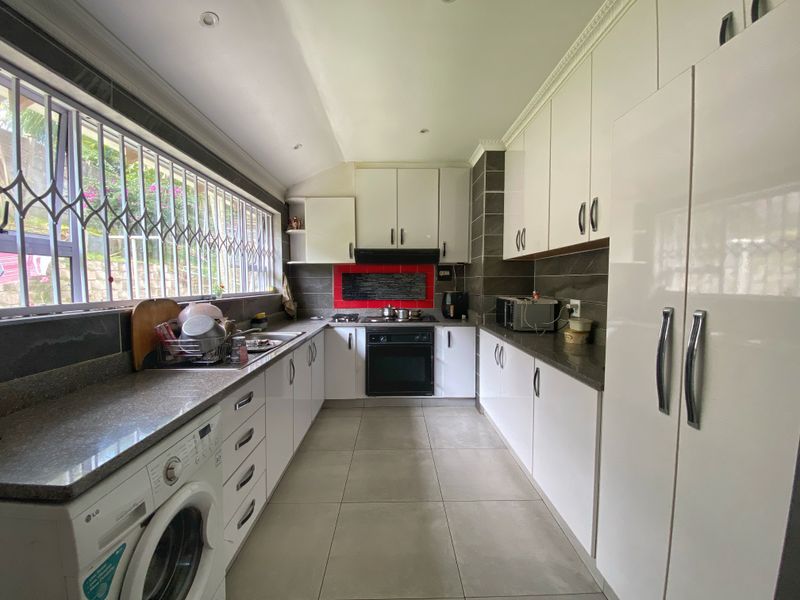 A functional kitchen featuring white cabinetry, stone countertops, integrated oven and hob, tiled flooring, and a large window with security bars.