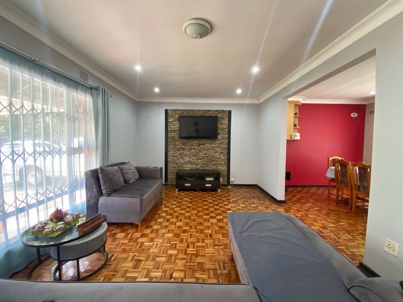 Open-plan living area featuring parquet flooring, a stone feature wall, and recessed lighting, flowing into an adjacent dining space with a bold accent wall.