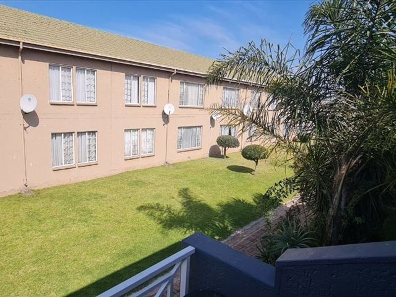 View of the apartment complex rear facade featuring a communal garden area and balcony access.