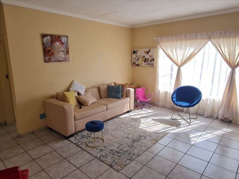 A living room featuring tiled flooring, coved ceilings, and a large window with security bars, offering a functional space with potential for cosmetic updates.