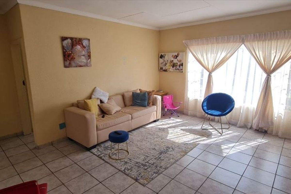 A living room featuring tiled flooring, coved ceilings, and a large window with security bars, offering a functional space with potential for cosmetic updates.