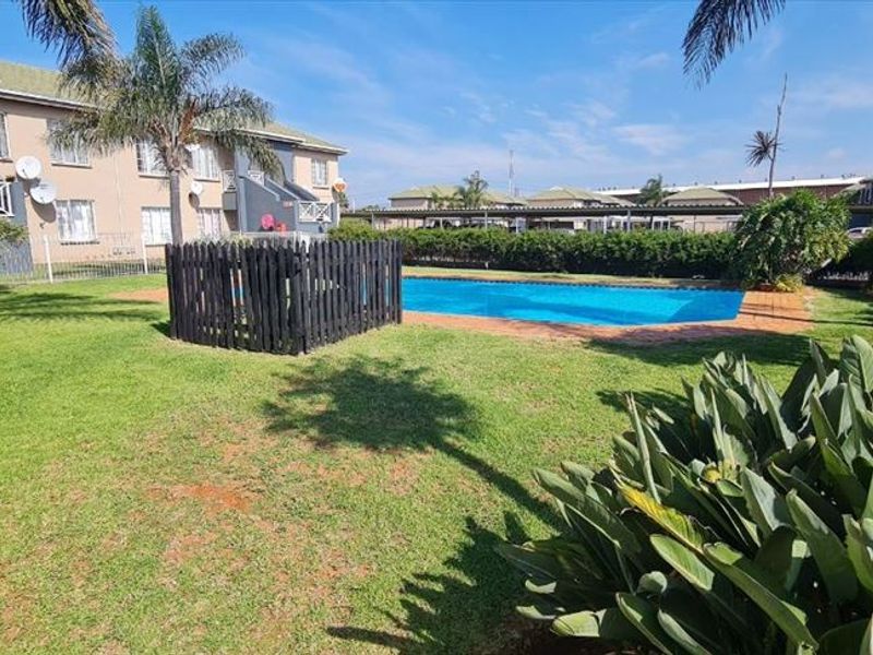 Communal outdoor area featuring a swimming pool set within a well-maintained garden and paved surrounds, serving the apartment complex.