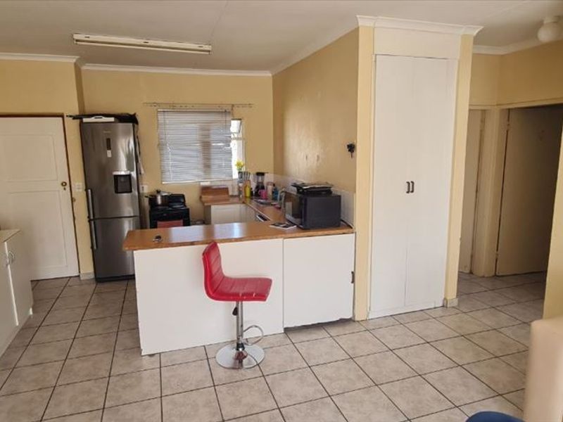 Open plan living and kitchen area featuring tiled flooring, built-in cabinetry, and a breakfast counter, offering a functional layout with potential for cosmetic updates.
