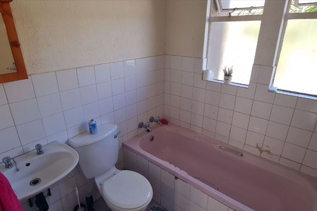 A dated bathroom featuring a pink bathtub, pedestal basin, and white wall tiles, offering potential for a modern renovation.