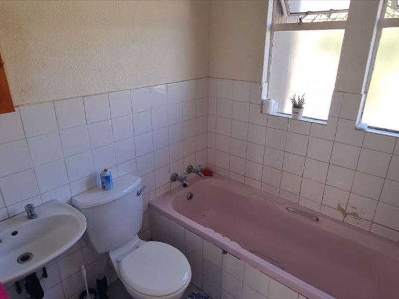 A dated bathroom featuring a pink bathtub, pedestal basin, and white wall tiles, offering potential for a modern renovation.