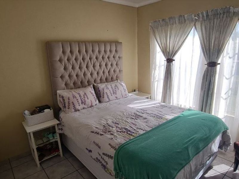A bedroom featuring tiled flooring and large windows with curtain rails, providing natural light and a functional layout.