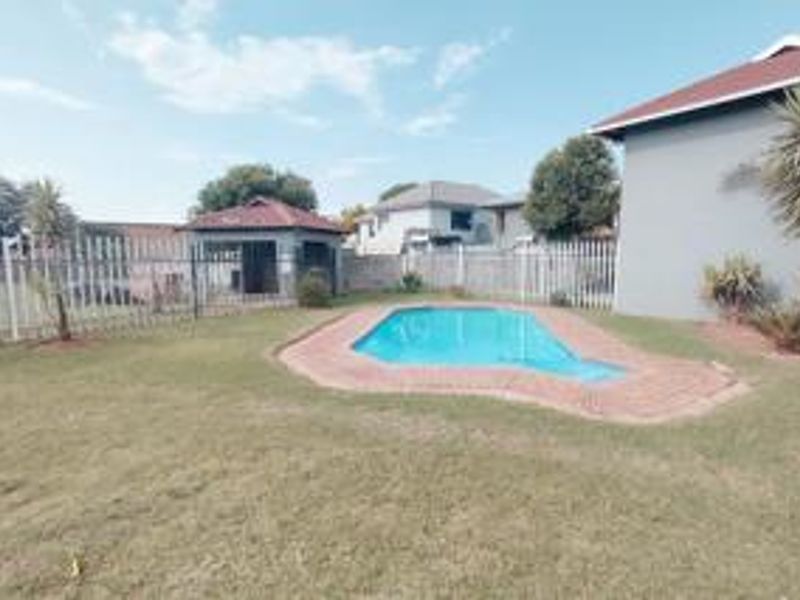 A backyard area featuring a swimming pool with brick coping, surrounded by a lawn and perimeter fencing, with a detached outbuilding in the background.