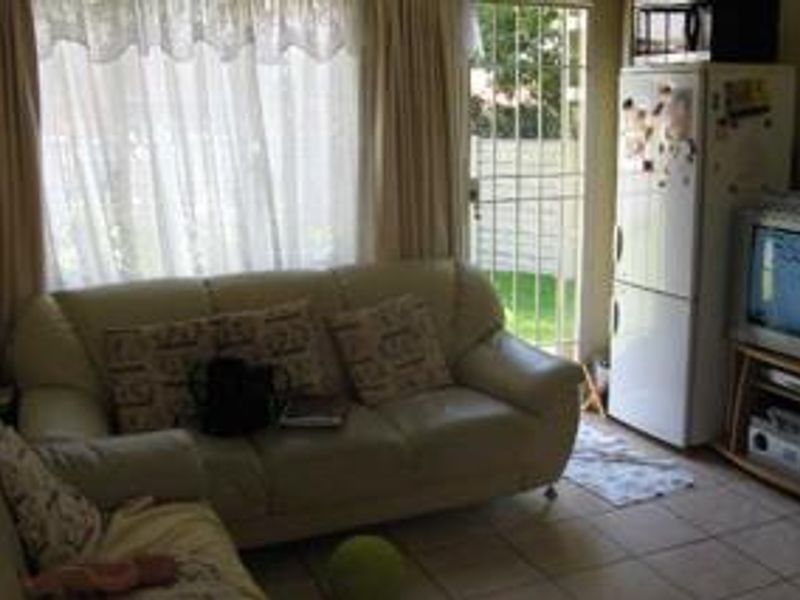 A living room area featuring tiled flooring, a large window with curtains, and a security gate leading to the exterior.