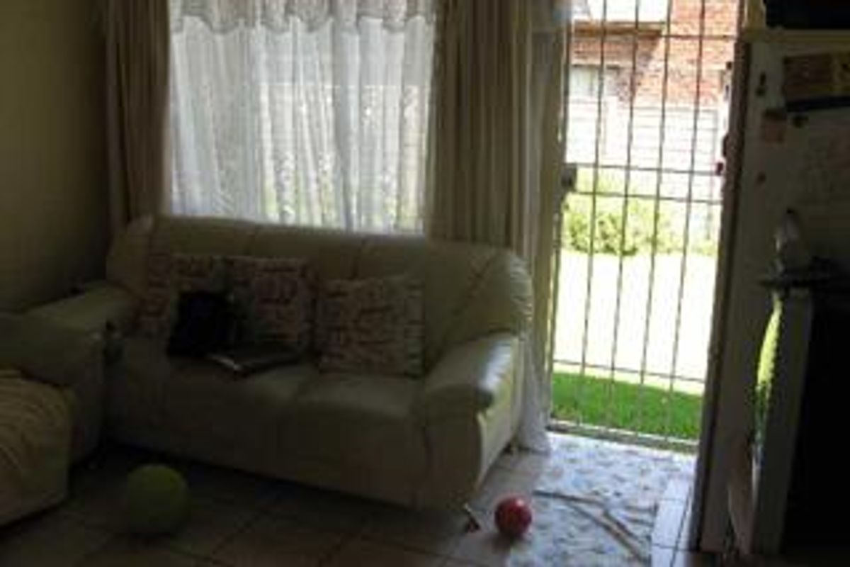 A living room area featuring tiled flooring and a security gate leading to the exterior garden space.