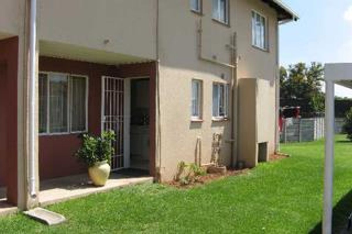 Rear view of the townhouse featuring a covered patio, security gate, built-in braai, and a private garden area.