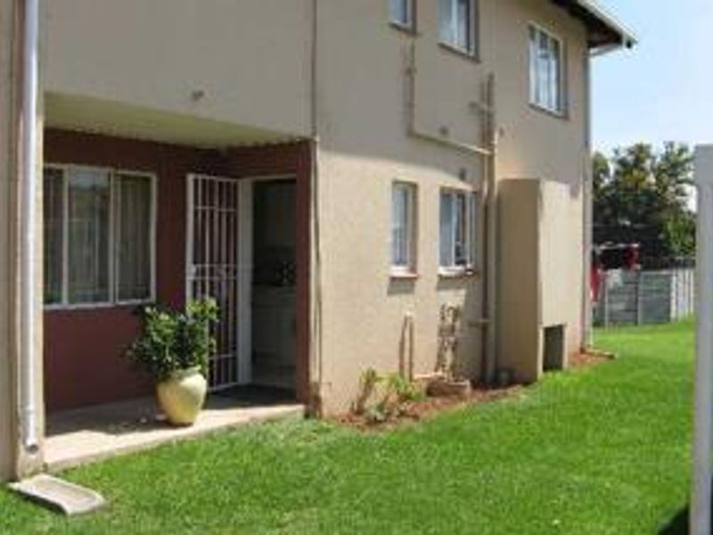 Rear view of the townhouse featuring a covered patio, security gate, built-in braai, and a private garden area.