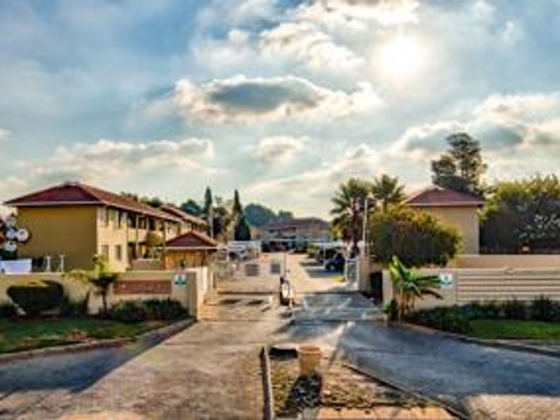 The front entrance of the townhouse complex featuring a secure gated access point, paved driveway, and established perimeter walls.