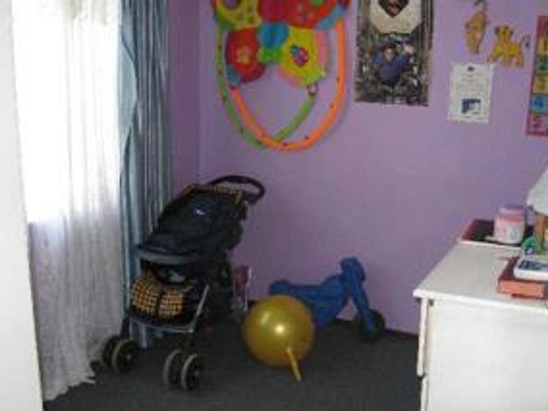 A bedroom featuring purple walls and carpeted flooring, currently utilized as a nursery or play area.