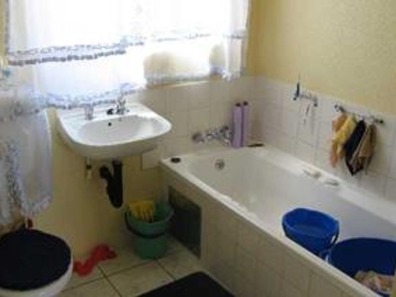 A dated bathroom featuring a built-in bathtub, wall-mounted basin, and tiled splashbacks, offering potential for a modern renovation.