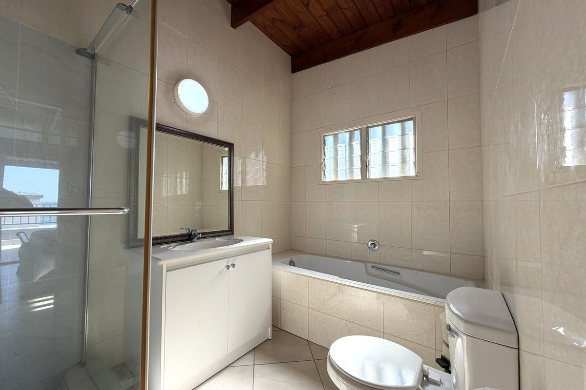 A functional bathroom featuring a shower enclosure, bathtub, vanity unit, and tiled finishes, complemented by a distinctive timber-beamed ceiling.