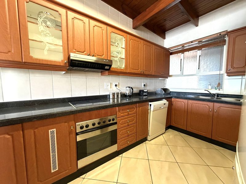 A functional kitchen featuring traditional wooden cabinetry, granite countertops, built-in oven, electric hob, and exposed timber ceiling beams.