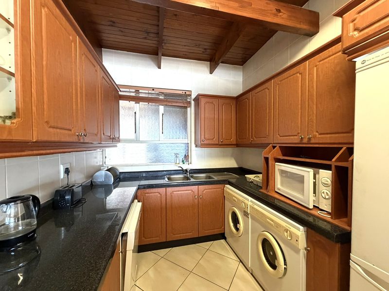 A functional kitchen featuring warm wooden cabinetry, granite countertops, a double basin sink, and distinctive exposed wooden ceiling beams.