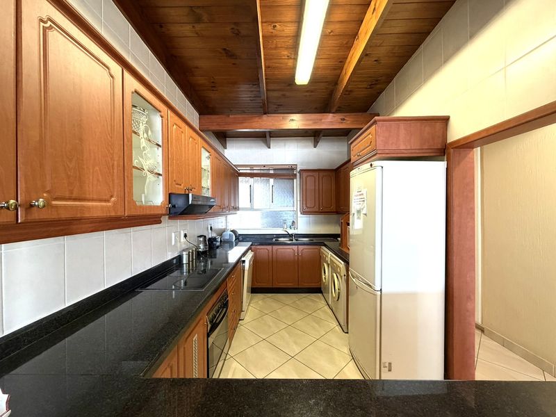 A functional kitchen featuring timber cabinetry, granite countertops, built-in appliances, and a distinctive timber beam ceiling with tiled flooring.