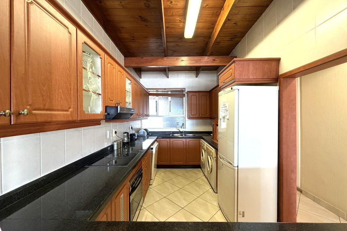 A functional kitchen featuring timber cabinetry, granite countertops, built-in appliances, and a distinctive timber beam ceiling with tiled flooring.