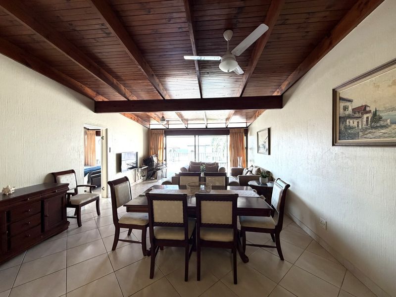 Spacious open-plan living and dining area featuring a high exposed timber beam ceiling, ceramic tiled flooring, and direct access to a patio.