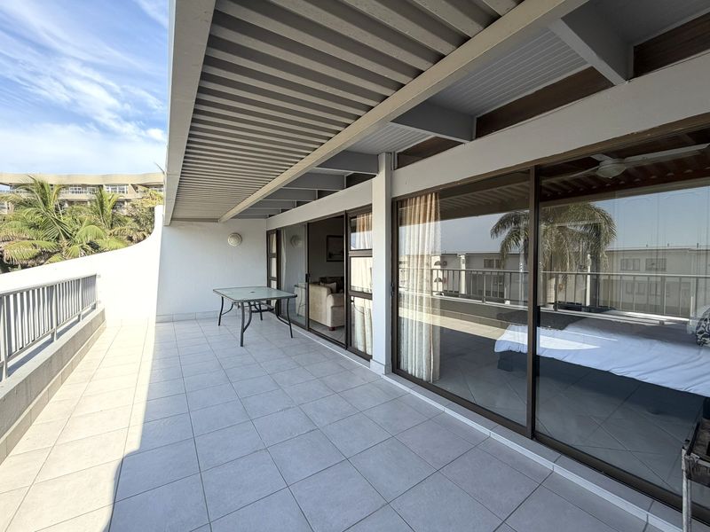 Spacious covered balcony featuring tiled flooring, metal railings, and large sliding glass doors providing seamless indoor-outdoor flow.