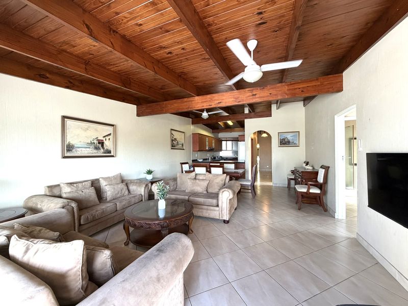 Spacious open-plan living and dining area featuring a distinctive exposed timber beam ceiling, tiled flooring, and seamless flow into the kitchen.