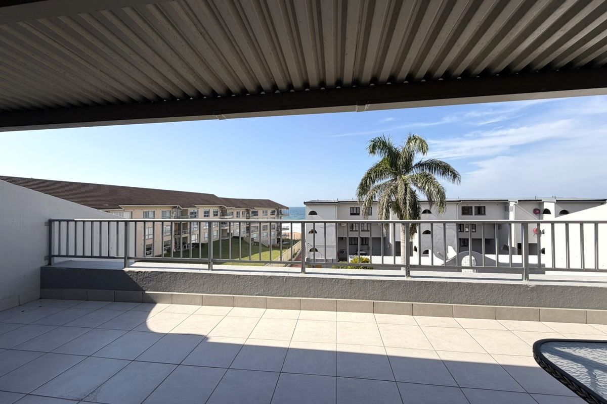 Spacious covered balcony featuring tiled flooring and a metal balustrade, offering pleasant views of the surrounding complex and distant ocean.