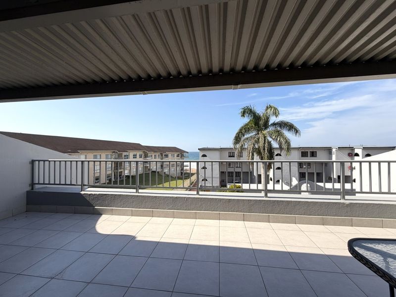 Spacious covered balcony featuring tiled flooring and a metal balustrade, offering pleasant views of the surrounding complex and distant ocean.