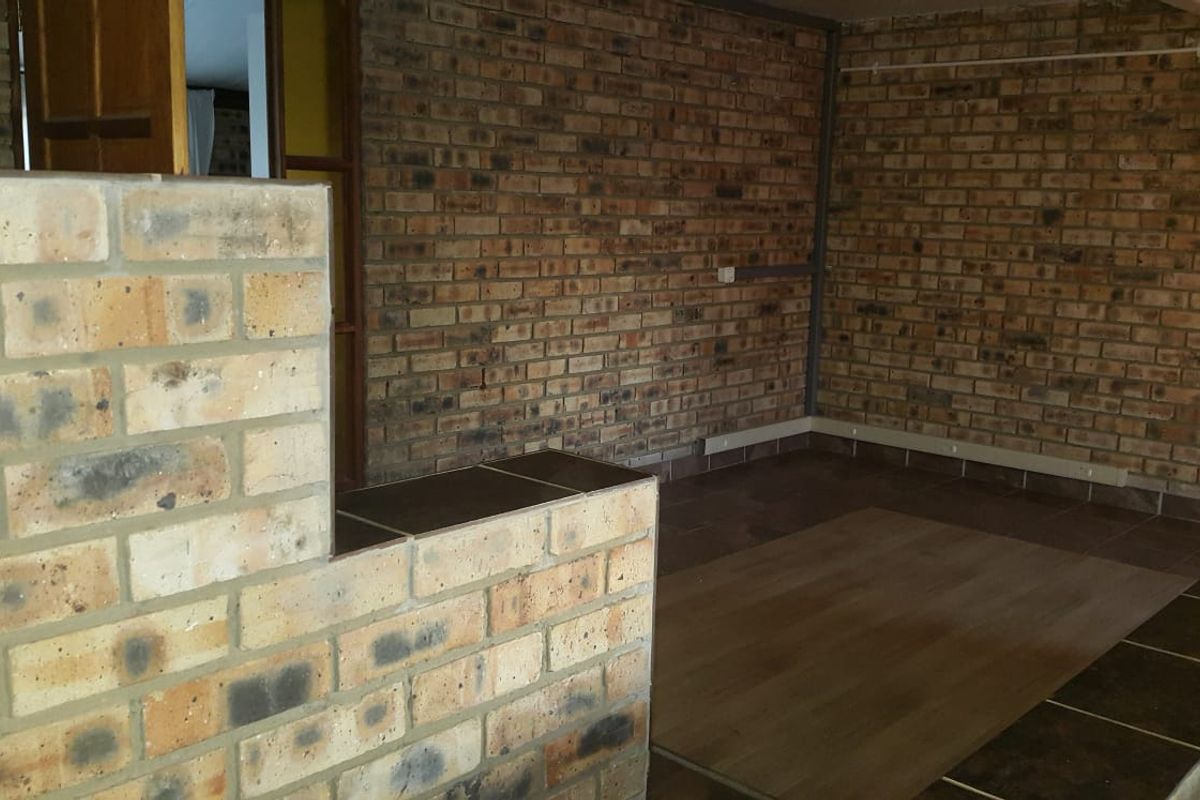 An empty living area featuring exposed brick walls, mixed flooring surfaces, and a wall-mounted light fixture, offering a rustic foundation for renovation.