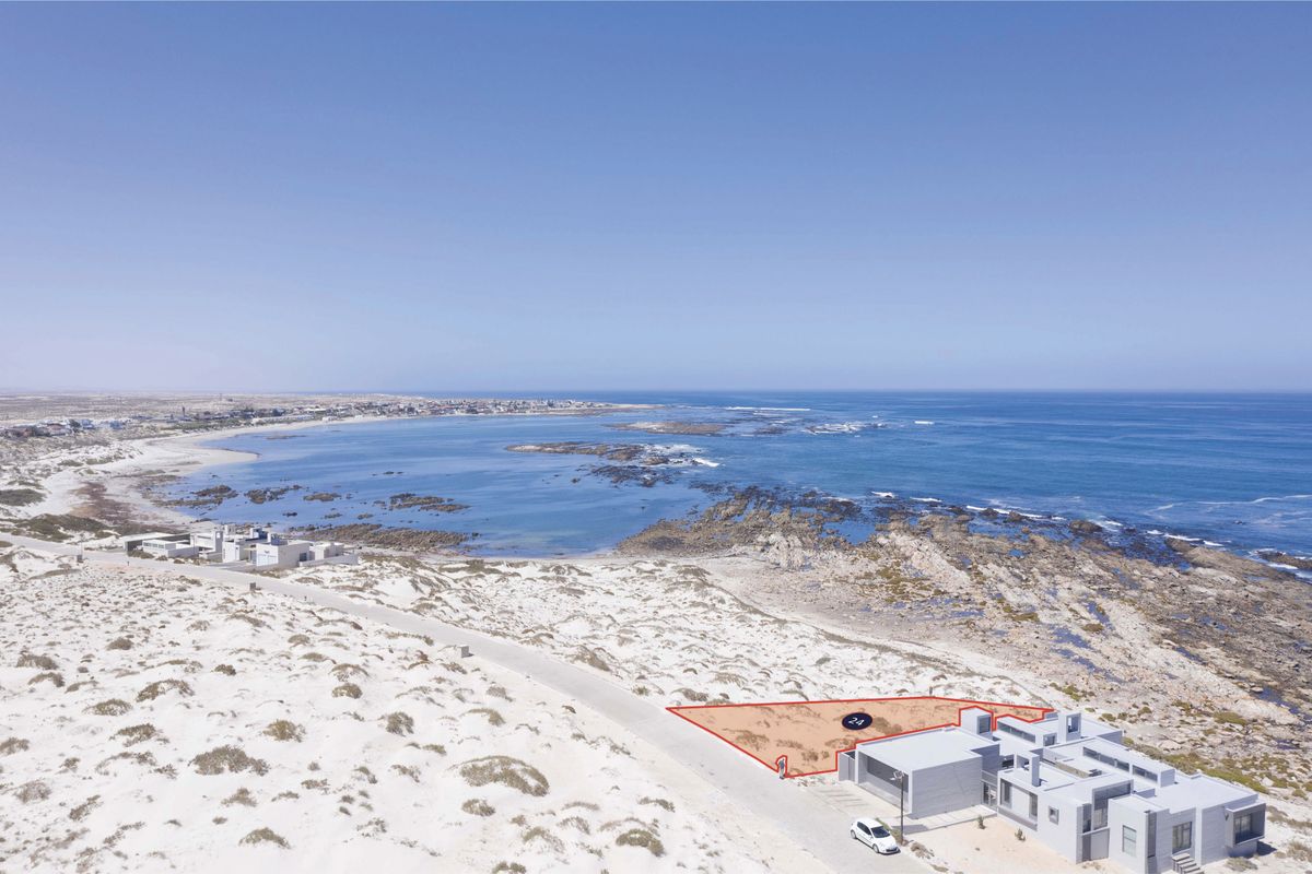 An aerial view of a vacant coastal residential plot, highlighting its prime location near the ocean and existing infrastructure.