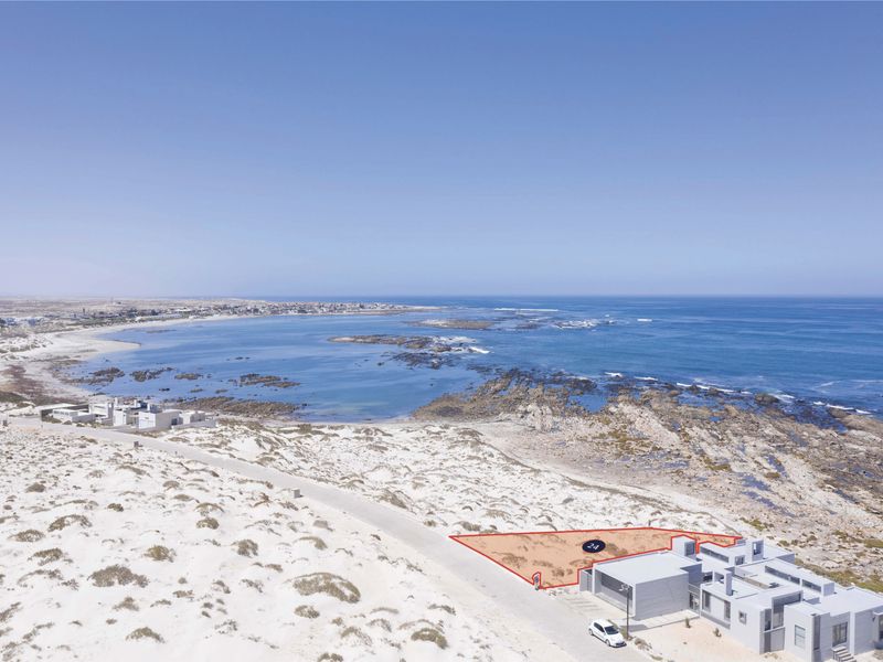An aerial view of a vacant coastal residential plot, highlighting its prime location near the ocean and existing infrastructure.