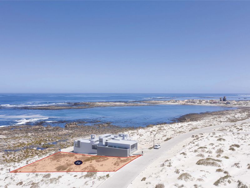 An aerial view of a vacant residential plot situated in a coastal location with direct road access and ocean views.