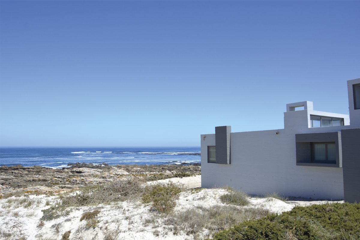 A modern coastal property exterior featuring clean masonry lines, situated directly along a rocky shoreline with expansive ocean views.