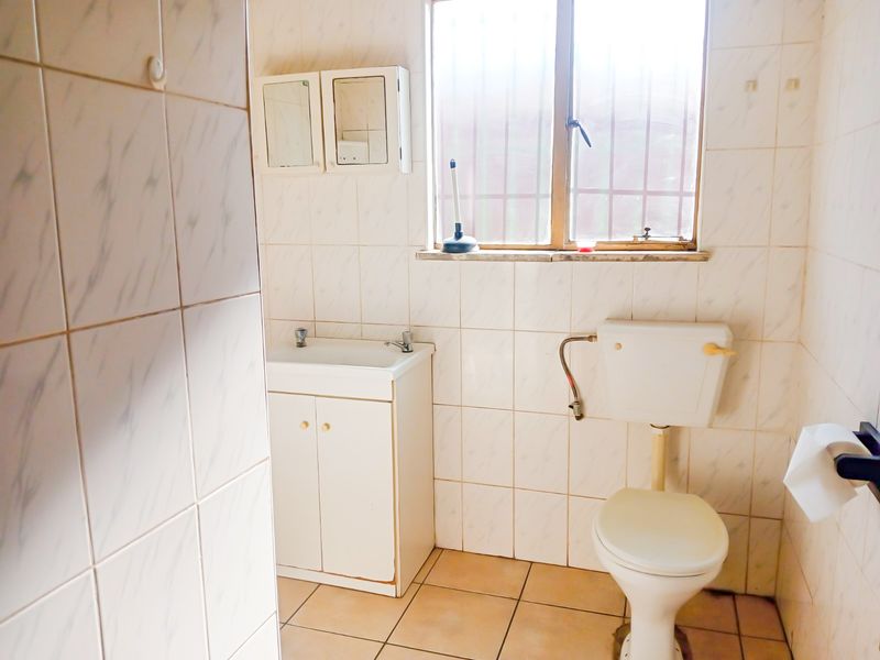 A functional bathroom featuring a vanity cabinet, ceramic basin, and toilet, finished with tiled walls and flooring. Ready for a modern update.