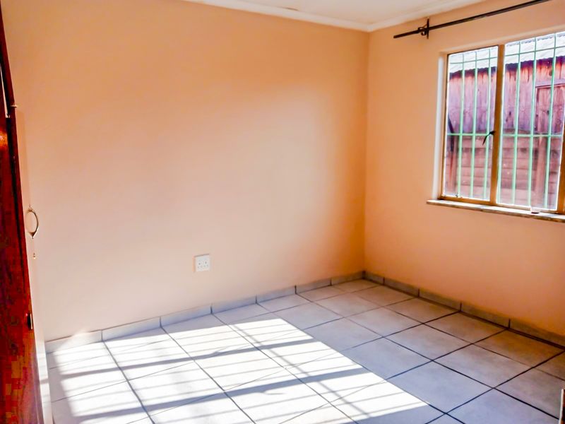 A vacant bedroom featuring neutral walls, tiled flooring, and a window fitted with security bars.