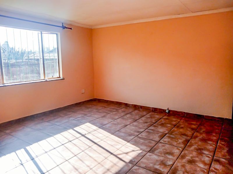 An empty bedroom featuring tiled flooring and a window with security bars, offering a blank canvas for interior design updates.