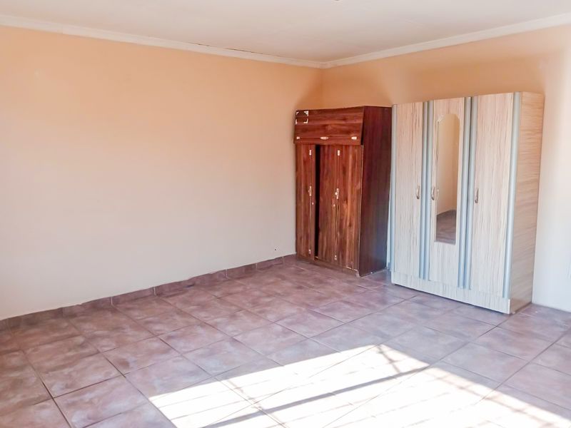 A spacious, empty bedroom featuring neutral wall tones, tiled flooring, and a coved ceiling, providing a blank canvas for personalization.