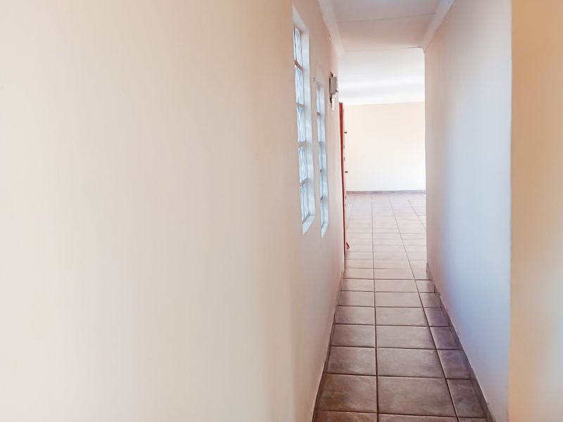 A bright, empty hallway featuring tiled flooring and glass block windows, leading into an open living space.