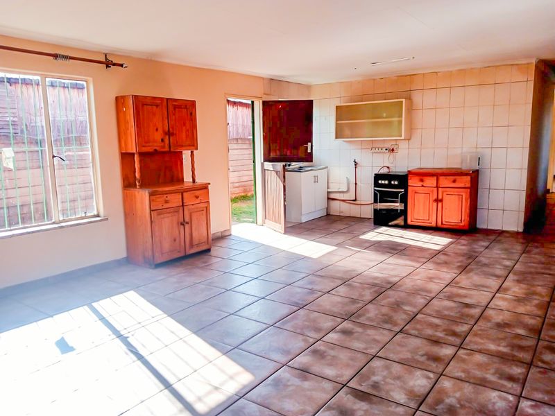 A functional kitchen area featuring tiled flooring, tiled splashbacks, and basic cabinetry, offering a blank canvas for potential modern updates and renovation.