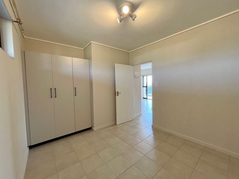 A clean, empty bedroom featuring neutral tiled flooring and built-in cupboards, offering a bright and versatile space ready for personalization.