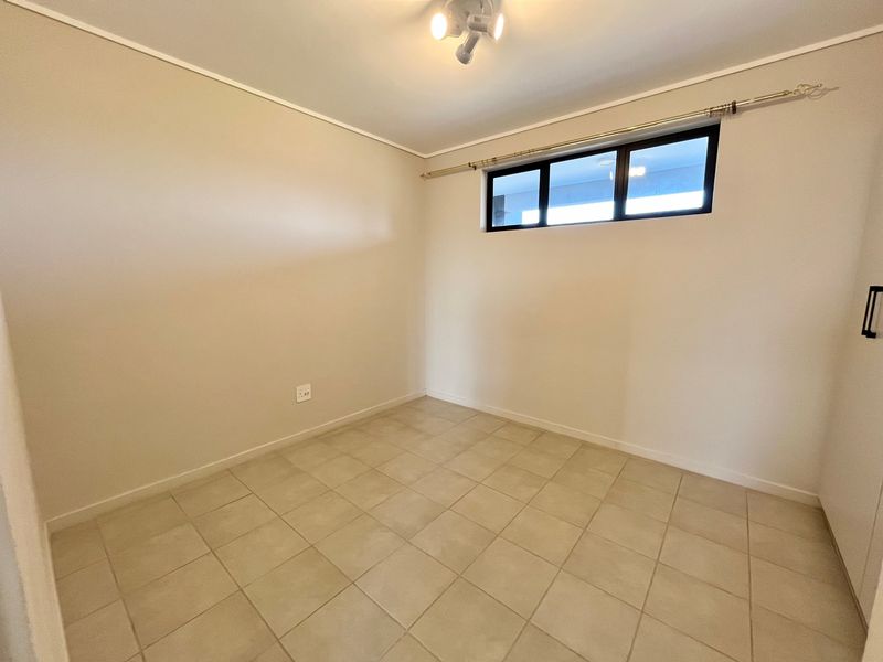 A clean, empty bedroom featuring neutral tiled flooring, a built-in cupboard, and a horizontal window providing natural light.
