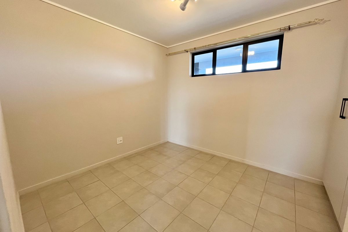 A clean, empty bedroom featuring neutral tiled flooring, a built-in cupboard, and a horizontal window providing natural light.