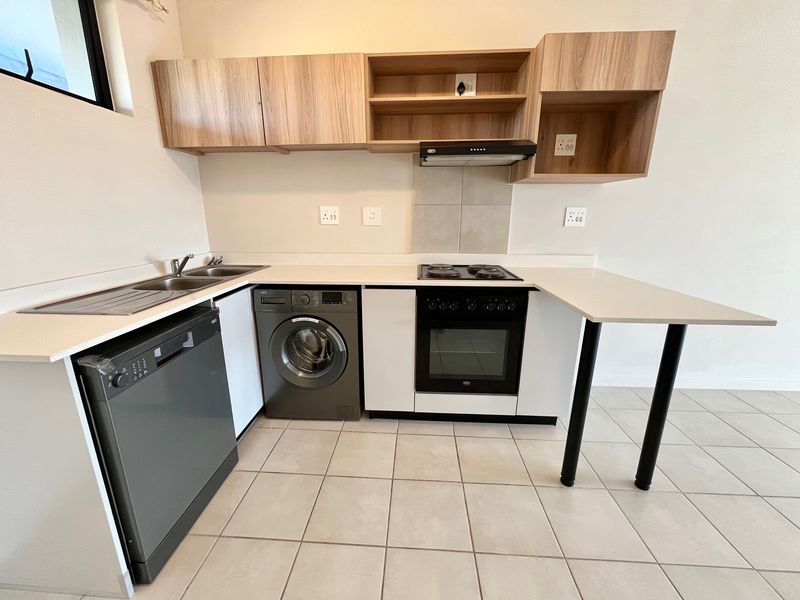 Modern kitchen featuring light wood-tone cabinetry, white countertops, a breakfast bar, and integrated appliances including an oven, hob, and extractor fan.
