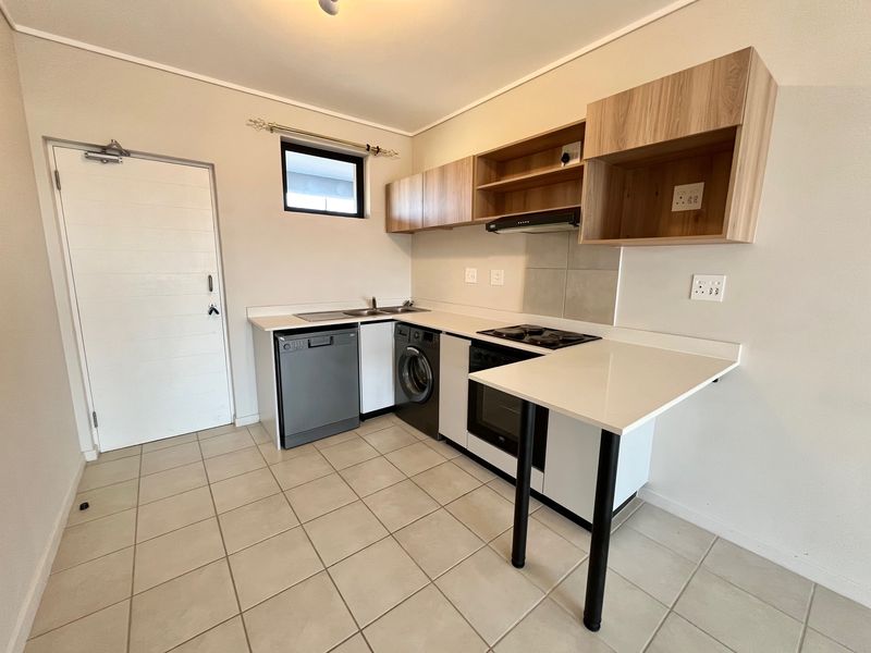 A clean, modern kitchen featuring light wood-tone cabinetry, stone countertops, integrated appliances, and neutral tiled flooring.